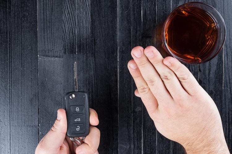 closeup of hand holding car key and refusing glass of liquor - harm reduction