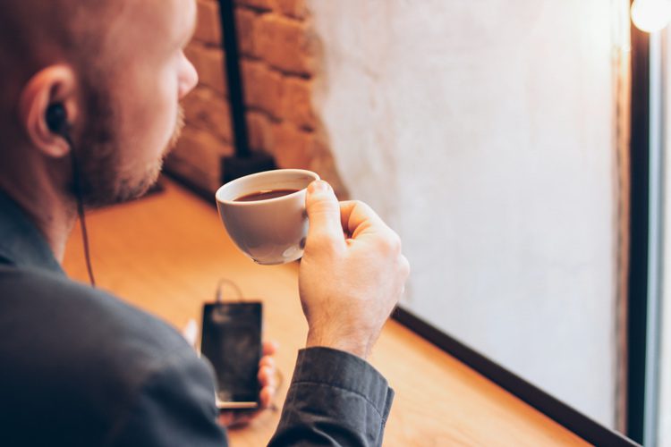 man drinking coffee and listening to headphones on phone - podcasts