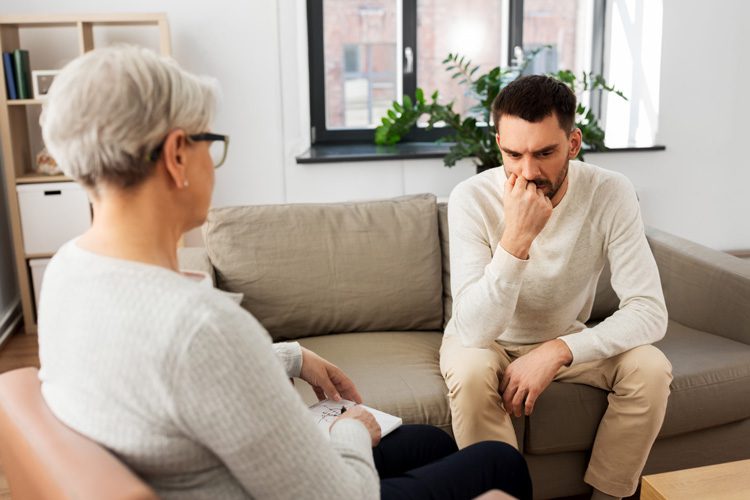 man in therapy session with older female counselor - cognitive behavioral therapy