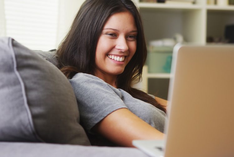 smiling woman watching video on laptop at home - encouragement