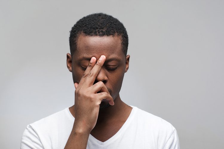 African American man in white tee shirt with hand on face looking stressed - negative self-talk