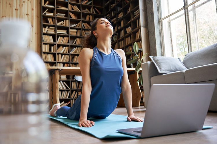 woman doing yoga at home in front of laptop - yoga and recovery