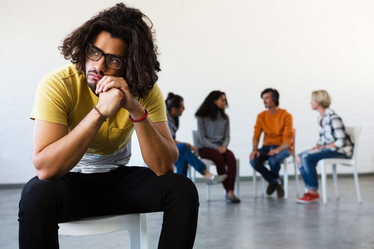 upset looking man outside of group circle at group therapy setting - anxiety and substance use