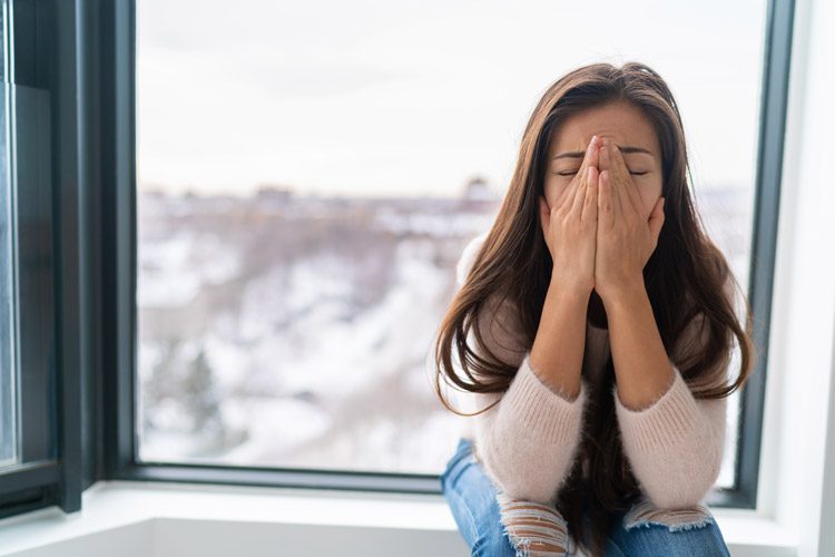 Seasonal Affective Disorder and Addiction Recovery, sad looking woman sitting on window sill in winter - seasonal affective disorder