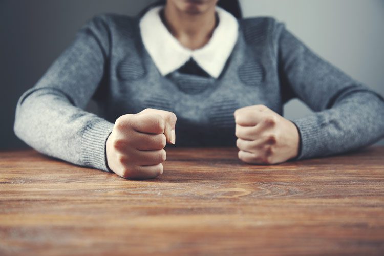 cropped shot of woman with fisted hands sitting at wooden table - anger