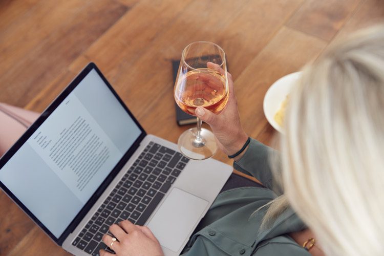 woman using her laptop and drinking a glass of wine - high-functioning alcoholics