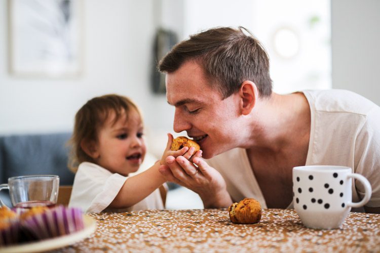young dad with his toddler daughter eating mini muffins together - parenting in recovery