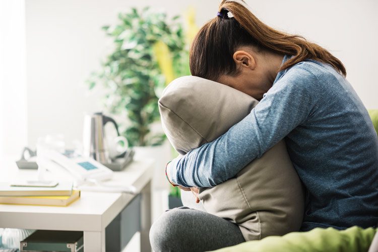 woman sitting on couch with her face buried in a pillow - Ativan