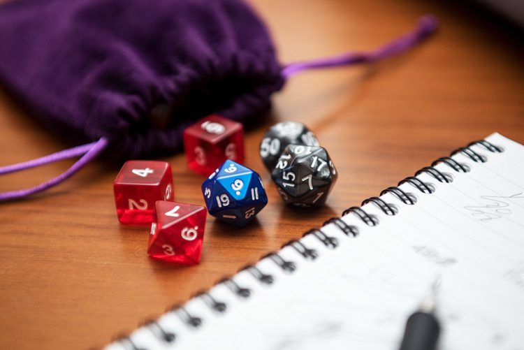 closeup of gaming dice and purple velvet pouch next to a journal with a pen - hobbies