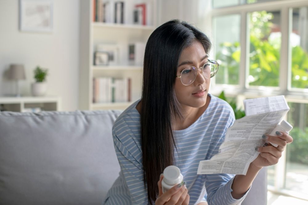 Woman sitting on a couch reading prescription instructions while holding a medication bottle
